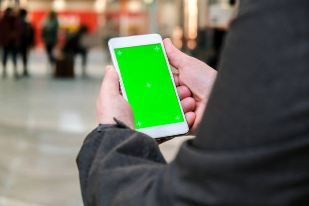 istock Female hands using mobile phone with green screen. Chroma key. Mobile app on Shopping Mall. People walking on background 1313412590