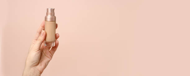 istock Hand holding makeup liquid found, Applying foundation for makeup. Woman's hands with neutral manicure holding bottle of concealer or toner foundation, copy space, banner, flyer 1313412599