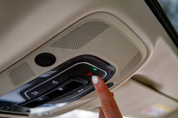 female driver's finger presses the sos button on the ceiling panel of a modern car stock photo