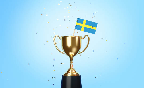 istock Championship Concept - Star Shaped Confetti Falling Onto A Gold Cup In Which Tiny Swedish Flag Sitting Before Blue Background 1313419439