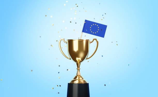 istock Championship Concept - Star Shaped Confetti Falling Onto A Gold Cup In Which Tiny EU Flag Sitting Before Blue Background 1313420043