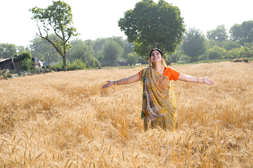 Happy rural woman with arms outstretched in agricultural field