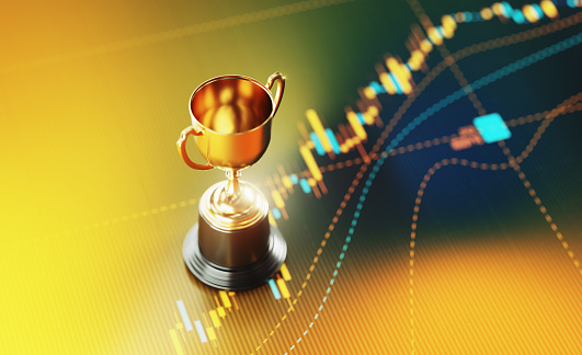 Gold trophy sitting on yellow financial graph background. Horizontal composition with selective focus and copy space. Investment, stock market data and finance concept.