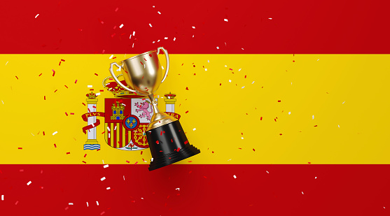 Colorful confetti falling onto a gold cup sitting over Spanish flag background. Horizontal composition with copy space. Front view. Championship concept.