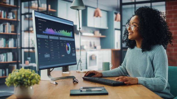 latina spécialiste féminine travaillant sur l’ordinateur de bureau au salon à la maison tout en s’asseyant à une table.  freelance female fait de l’analyse de marché et crée un rapport avec des graphiques pour les clients et l’employeur. - stock market data finance chart home finances photos et images de collection