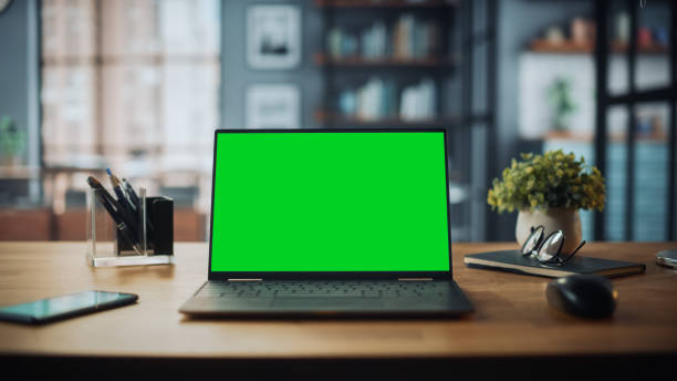 istock Laptop Computer with Mock Up Green Screen Display Standing on the Table in Cozy Living Room. In the Background Stylish Modern Bright Home Office Studio During Day with Big Cityscape Window. 1313422785