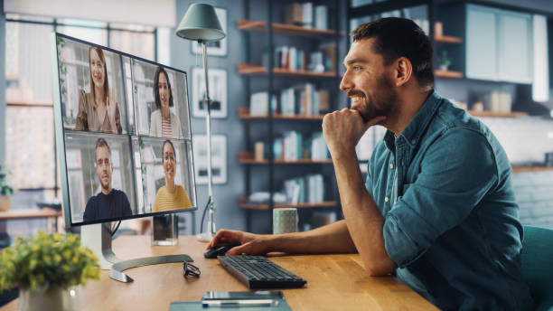 istock Handsome Caucasian Specialist Making a Video Call on Desktop Computer at Home Living Room while Sitting at Table. Freelancer Working From Home and Talking to Colleagues and Clients Over the Internet. 1313422834