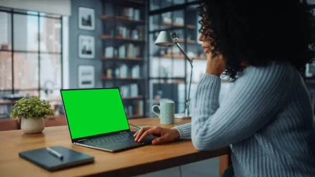 Close Up Female Specialist Working on Laptop with Green Screen Mock Up Display at Home Living Room while Sitting at a Table. Freelancer Female Chatting Over the Internet on Social Networks.