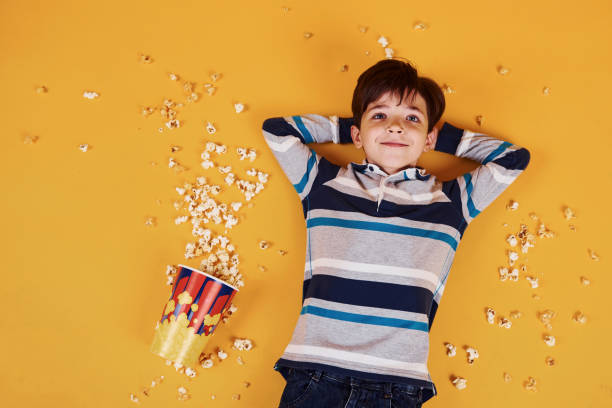 Cute little boy with popcorn lying down on the yellow floor.