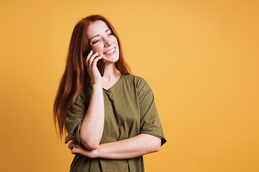 happy laughing young woman talking on her smartphone or mobile cell phone - yellow color background with copy space