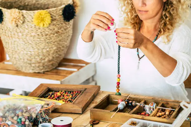 Photo of Woman at home make handmade jewellery. Box with beads on old wooden table. view with woman hands - tutorial to learn how to make bracelets and jewellery online and alternative home job