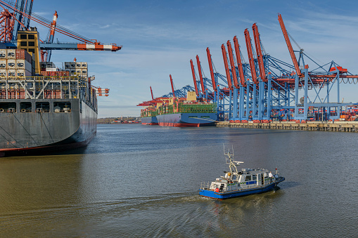 View of the container terminal in Hamburg, loading and unloading of various shipping container and police boat in the foreground. Seaport on the river Elbe in Hamburg.