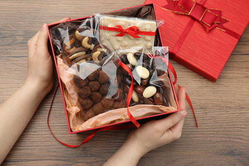 Woman with gift box of chocolate and sweets at wooden table, closeup