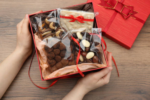 woman with gift box of chocolate and sweets at wooden table, closeup - chocolate candy gift package chocolate imagens e fotografias de stock