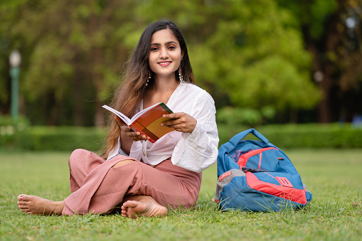 Outdoor image of Young Asian/Indian female College Student studying at park inside campus. She is holding books and looking at camera.
