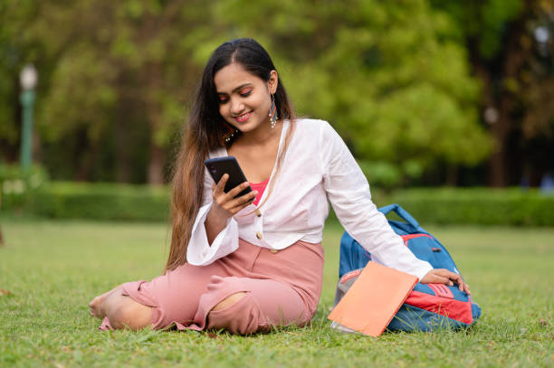 istock Young female student using mobile phone at park in campus 1313430535