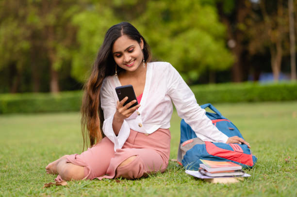 istock Young female student using mobile phone at park in campus 1313430603