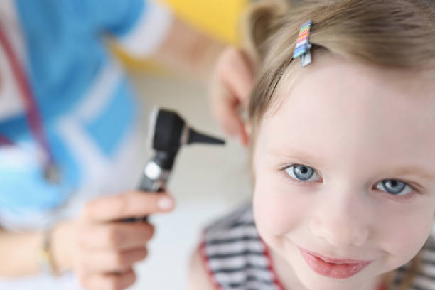 doctor examining ear with otoscope for little smiling girl - young ears imagens e fotografias de stock