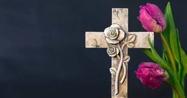 Ornate religious cross and fresh purple spring tulip flowers. Churches and funeral concept. Copy space on right hand side. Funeral symbol. Mourn and Condolence card concept. End of life.