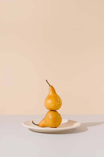 istock Yellow pears balancing on a ceramic plate against gray and beige background. Creative summer fruit sunlit arrangement. Minimal retro styled surreal food art concept. 1313436075
