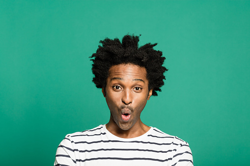 Studio portrait of funky afro american young man wearing striped t-shirt, looking at camera. Studio portrait on green background.