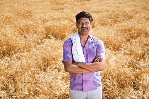 Happy rural farmer with arms crossed in agriculture field