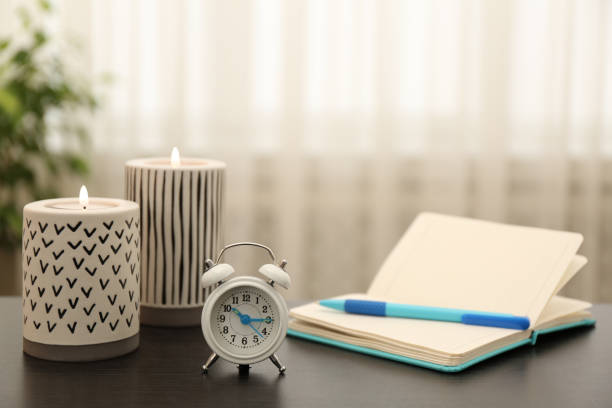 istock Notebook, alarm clock and burning candles on table indoors 1313437848