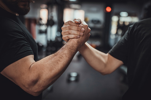 Two people, fitness trainer shaking hands with male client after god exercise in gym.