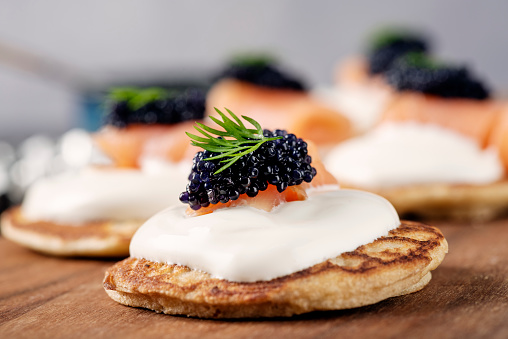 Homemade blinis made with; flour, buckwheat flour, egg yolks, yeast, milk and egg whites. Traditionally eaten with blinis you can create your own recipe, here shown with; creme fraiche, smoked salmon, caviar of course, topped with dill. Colour, horizontal format with some copy space.