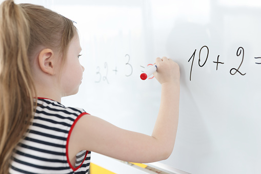 Little girl writes math examples on white board. Learning math for preschool kids concept