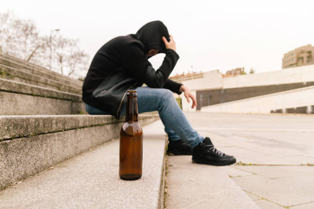 primo piano di una bottiglia di birra sul pavimento con un giovane ubriaco che piange con problemi e stress. concetto di problema sociale giovanile. - alcolismo foto e immagini stock