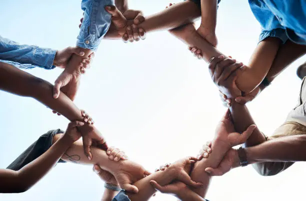 Photo of Low angle shot of an unrecognizable group of businesspeople standing together and holding each others arms in a circle