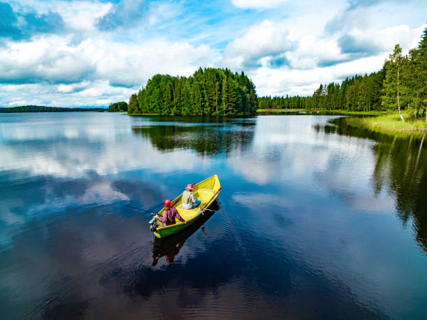 Aerial view of fishing boat with couple in blue summer lake in Finland Aerial view of fishing boat with young woman and man in blue summer lake in Finland rowing boat fishing stock pictures, royalty-free photos & images