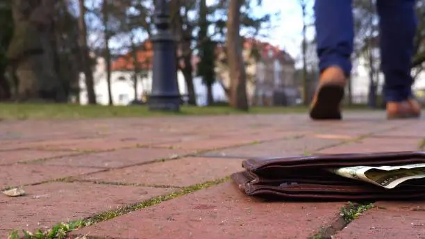 Caucasian Male Dropping A Brown Leather Wallet with Money Bill on the Ground in A City Park Close Up