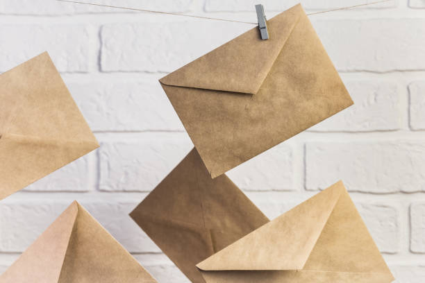 istock Concept postal communication background, several new paper brown craft letter envelopes hang on clothespins on a rope against a white wall background 1313453442