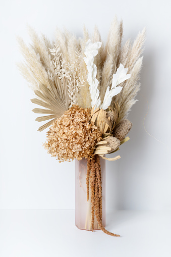 Modern dried flower arrangement in a pink vase. Including Banksia, Hydrangea, pampas grass, Palm Fronds, cream Ruscus leaves, and rust Amaranthus. Photographed on a white background.