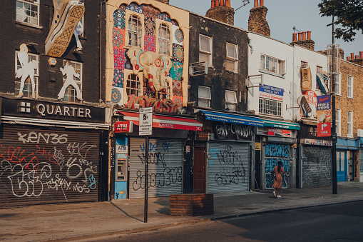 London, UK - August 12, 2020: Row of closed shops in Camden Town, London, an area famed for its market and nightlife and popular with tourists, teenagers and punks, woman walking past.