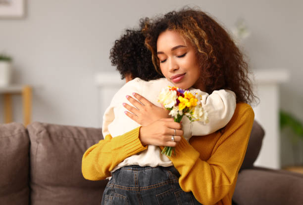 young mixed race woman mother with flower bouquet embracing son while getting congratulations on mother's day - 16936 imagens e fotografias de stock