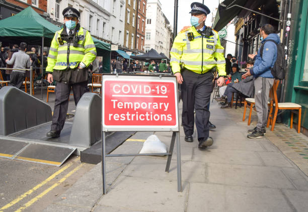 Police officers walk past a Covid-19 sign in Soho, London London, United Kingdom - 12th April 2021: Police officers walk past a Covid-19 Temporary Restrictions sign in Old Compton Street, Soho. Several streets in Central London have been blocked for traffic at certain times of the day to allow outdoor, al fresco seating for bars and restaurants during the coronavirus pandemic. covent garden photos stock pictures, royalty-free photos & images
