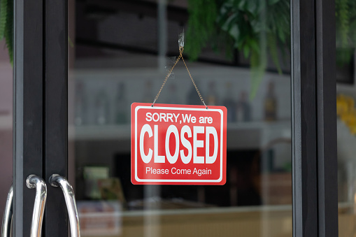 red close sign hang on glass door of shop. sorry we are closed.