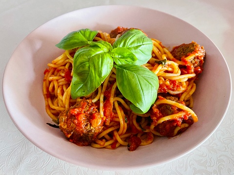 Spaghetti and meatballs in homemade marinara sauce garnish with fresh basil leaves.