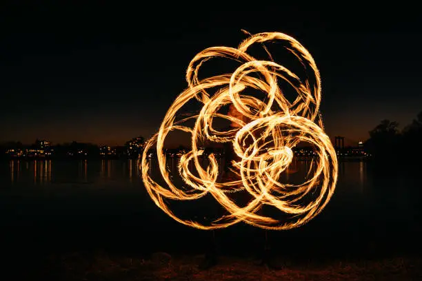 Male fire artist performing at night in front of a river and creating beautiful fire painting with flaming torches