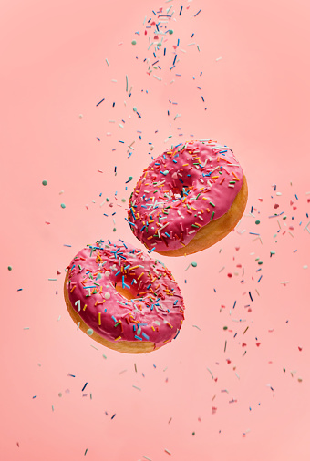 Two levitating donuts with sugar sprinkles on a pink background. Sweet donuts on a pink background.