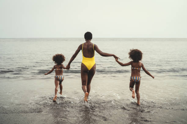 felice famiglia africana che corre in spiaggia durante le vacanze estive - persone afro-americane che si divertono in vacanza - i genitori amano e viaggiano concetto di stile di vita - family american culture african culture black foto e immagini stock
