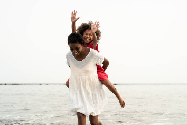 happy african family on the beach during summer holidays - afro american people having fun on vacation time - parents love and travel lifestyle concept - child caribbean black latin american and hispanic ethnicity imagens e fotografias de stock