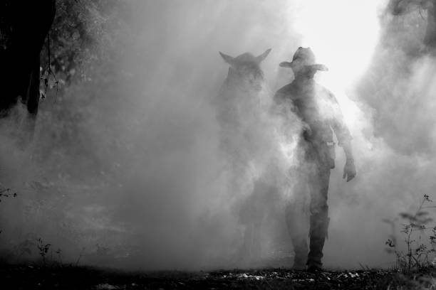 A black and white photo of a cowboy walking with a trusty horse. stock photo