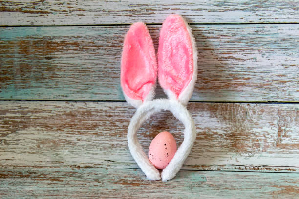 istock Single pink egg with floppy rabbit ears on a blue background. 1313481750