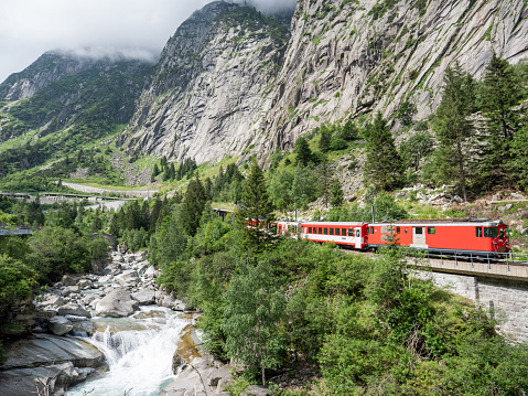 Red train on bridge crossing river in pine tree valley