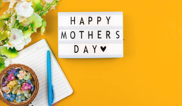 istock Happy Mothers Day greeting card concept with text message on a lightbox, spring and holiday workspace yellow background 1313484477