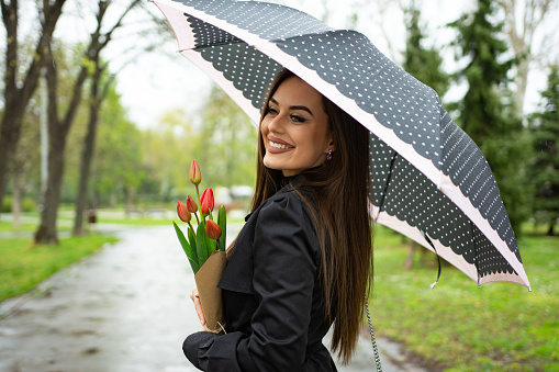 Business, weather, spring and people concept- young beautiful woman with umbrella in the park.